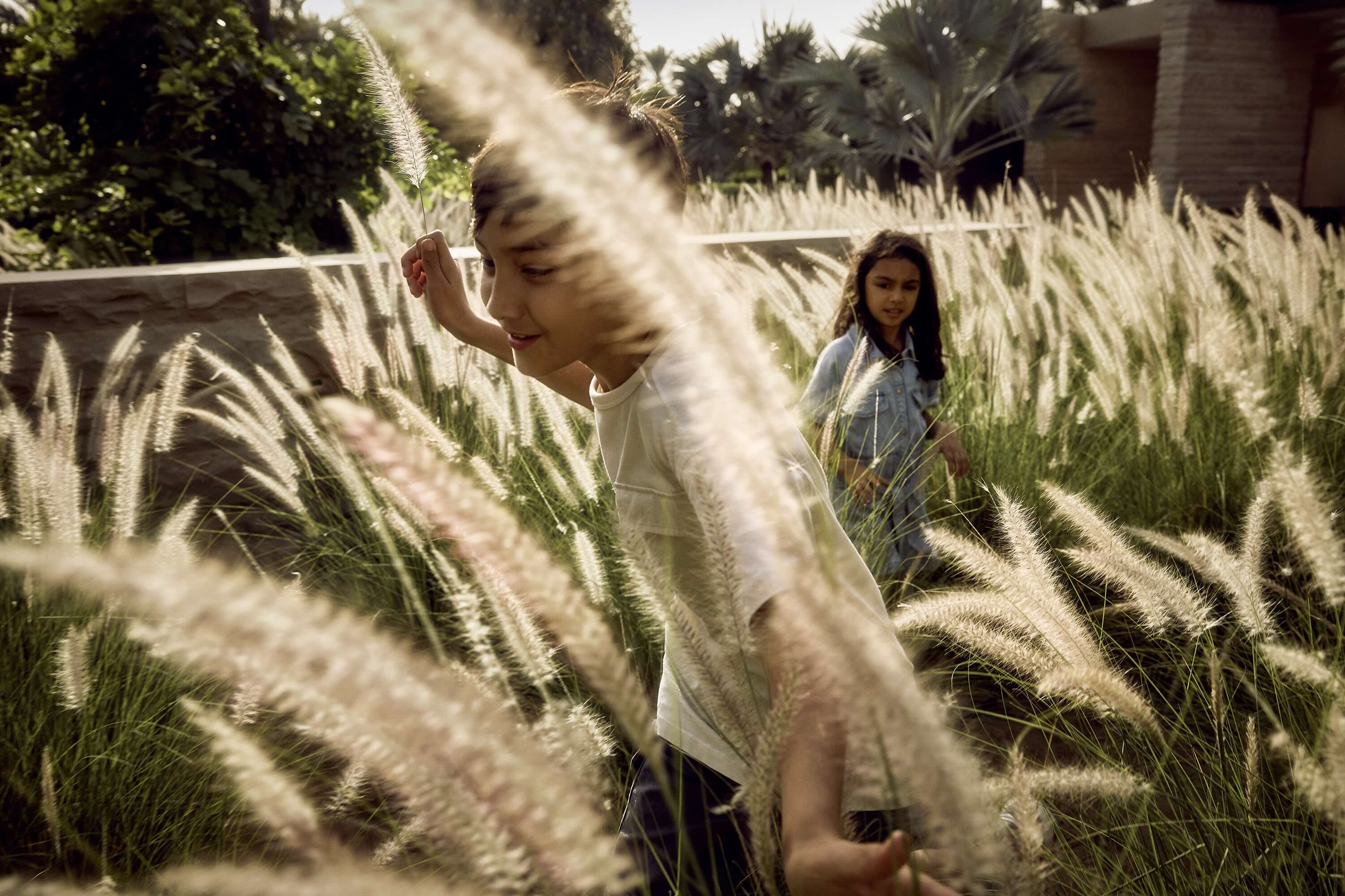 Two children exploring tall ornamental grasses in the landscaped gardens of the Athlon community