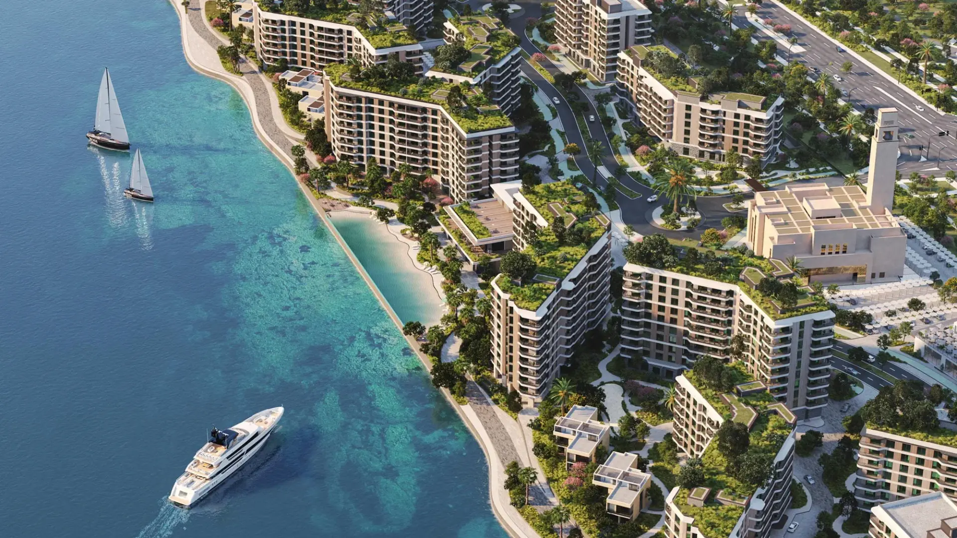 Aerial view of Gardenia Bay coastal residential development with mid-rise apartment buildings, landscaped rooftop gardens, tree-lined streets, a waterfront beach, and a landmark tower, with a yacht and sailboats on the water.