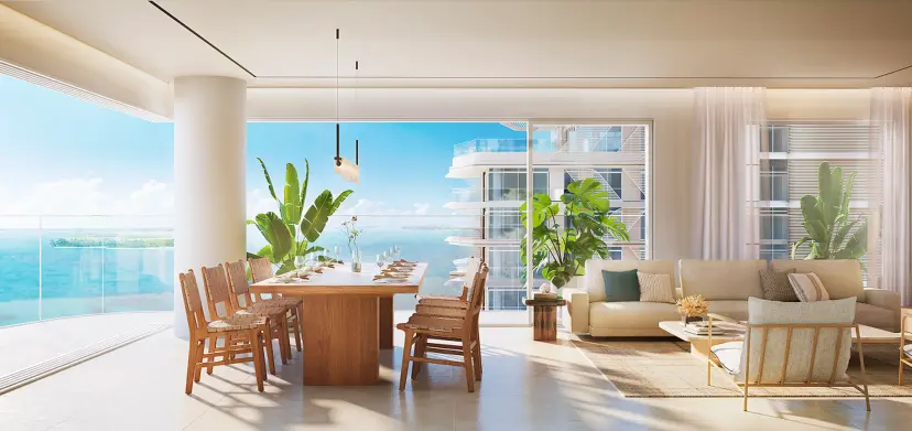Dining and living area at Fahid Beach Residences with a wood dining table set for six, woven chairs, tropical plants, and a beige sofa lounge area, opening onto a sea-view terrace.