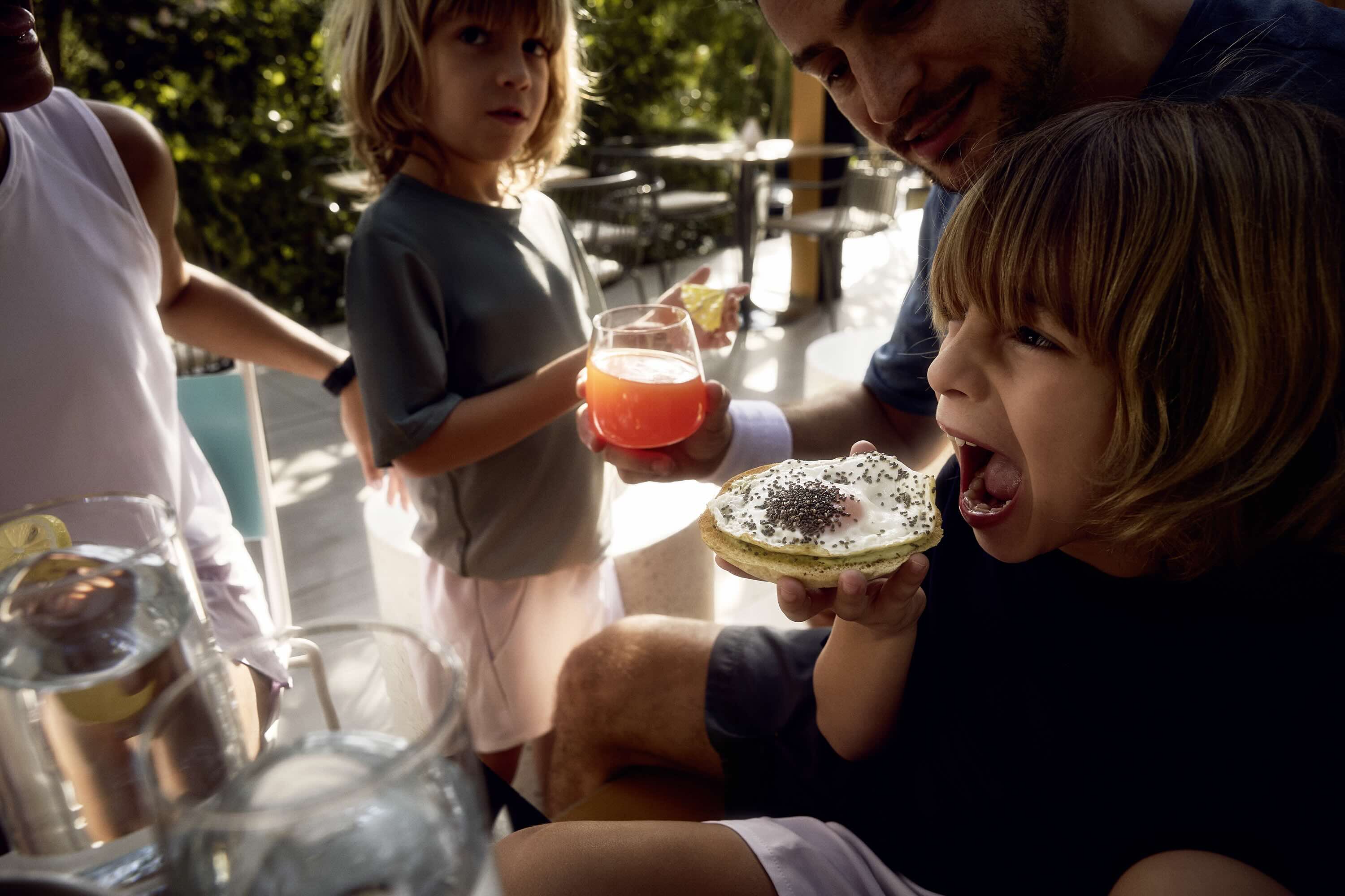 A family enjoying food and drinks outdoors in the Athlon community, with a child eating a snack and another holding a juice drink