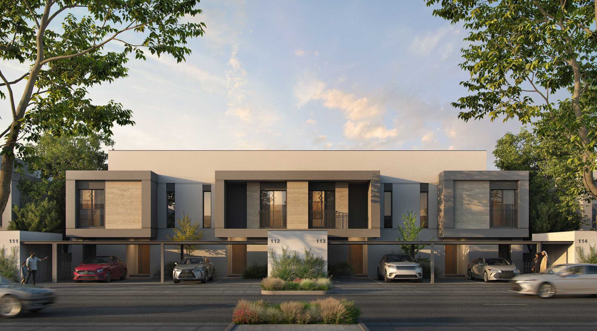 Front facade of Yas Acres The Orchids townhouses, with covered carports, cars parked below each unit, and landscaped trees framing the street view at dusk.